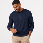 Man wearing a navy blue sweater and beige pants on a light gray background